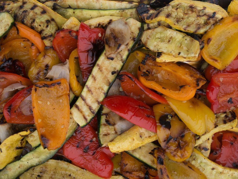 "Feast your eyes on this vibrant tableau of grilled summer bounty, filling the frame from edge to edge. A medley of zucchini, summer squash, and bell peppers in a rainbow of red, orange, and yellow join forces with caramelized onions. Each vegetable bears the distinct grill marks of a barbecue, adding a smoky depth to their natural sweetness. It's a celebration of color, texture, and flavor, all captured in one tantalizing photograph."